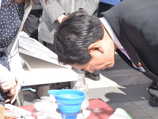 堀田の勧めでペットボトル顕微鏡を覗く下村文部科学大臣